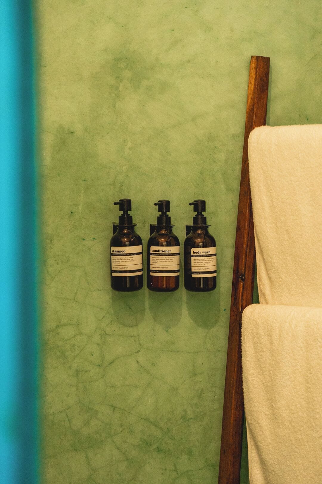 Trois bouteilles de shampoing, d’après-shampoing et de gel douche, posées sur une surface verte à texture.