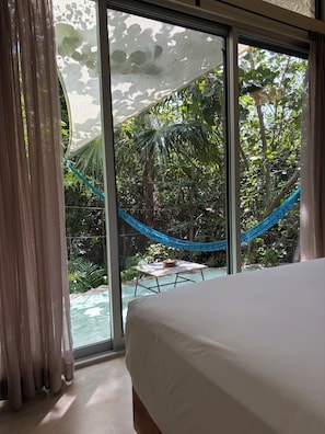 A bedroom with a large window overlooking a pool and lush greenery.