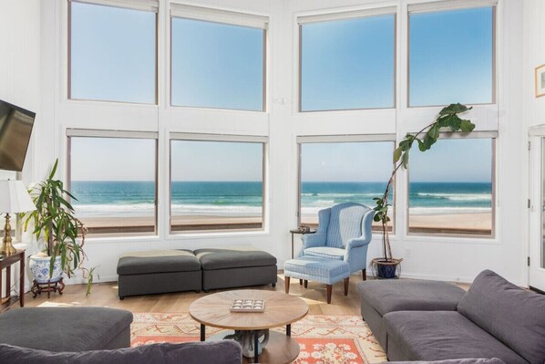 A living room with large windows, a grey sofa, a blue armchair, a small table, and a potted plant.