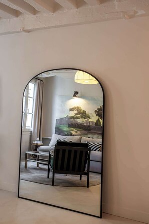 Quarto com um espelho grande refletindo uma pintura de paisagem, um sofá e um abajur.