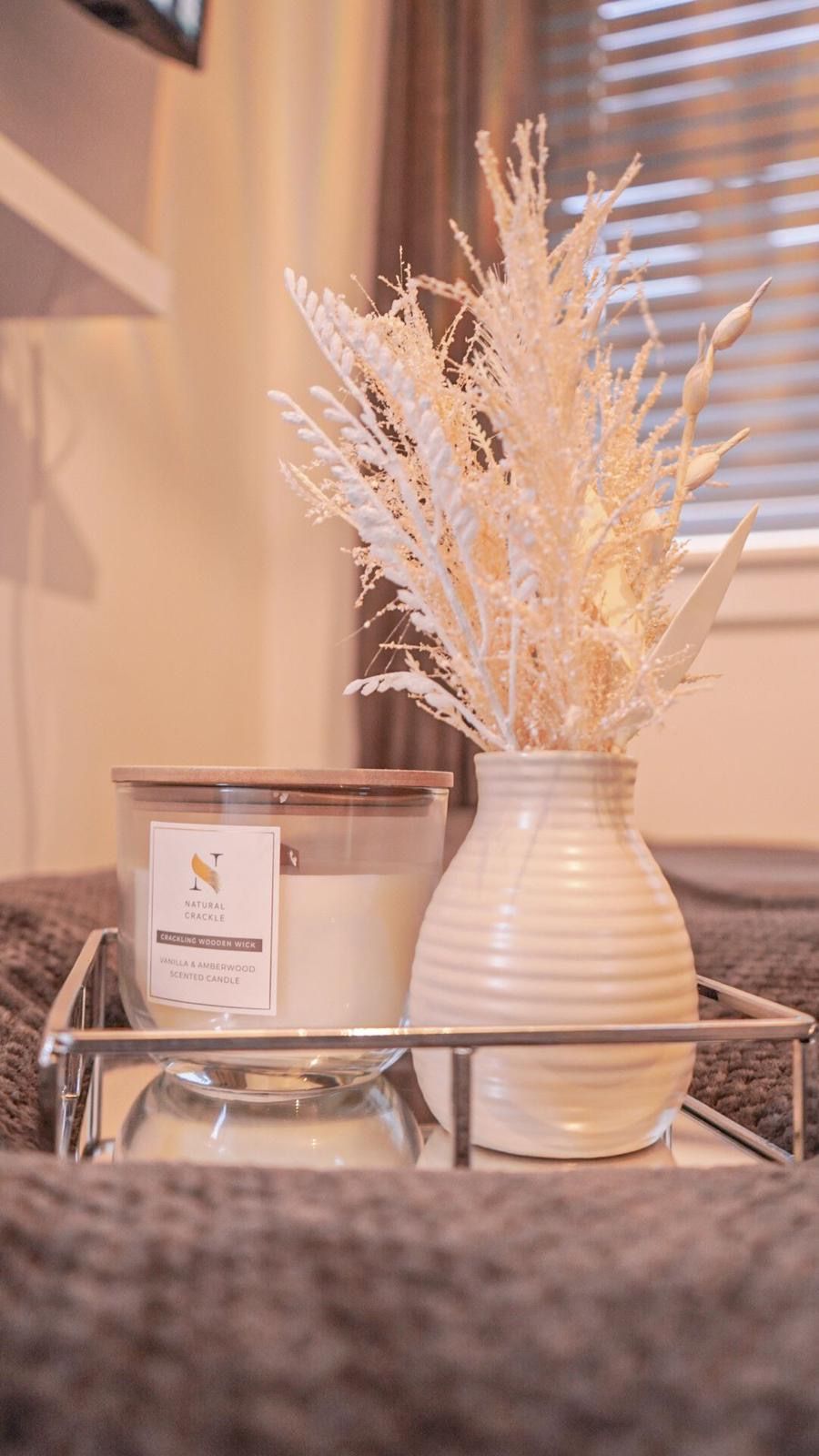 A candle and a vase with dried plants on a tray.