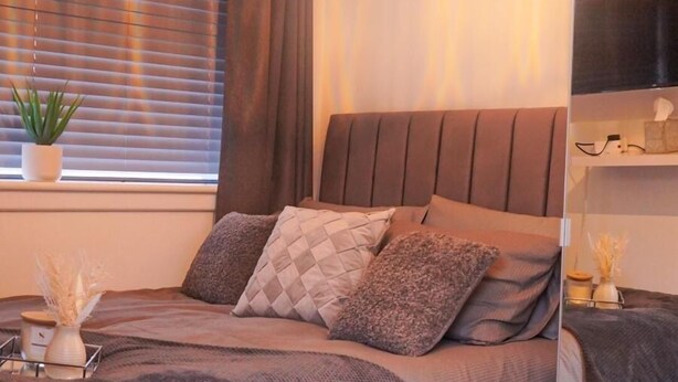 Ein modernes Schlafzimmer mit einem großen Bett, einem Spiegel, einer Topfpflanze und einem Fernseher auf einem Regal.