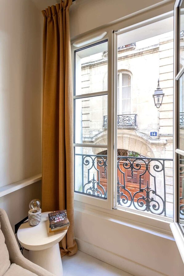 Habitación de esquina con un ventanal grande, una mesita con un libro y un objeto decorativo, y una cortina.
