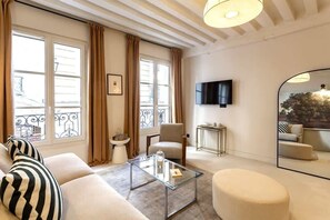 Una sala de estar moderna con un sofá, un reposapiés, una mesa de centro de vidrio y un televisor montado en la pared.