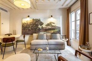 A modern living room with a sofa, chairs, a glass coffee table, and a painting on the wall.