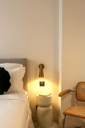 Una habitación de hotel con cama, mesita de noche con lámpara, una silla y un inodoro.