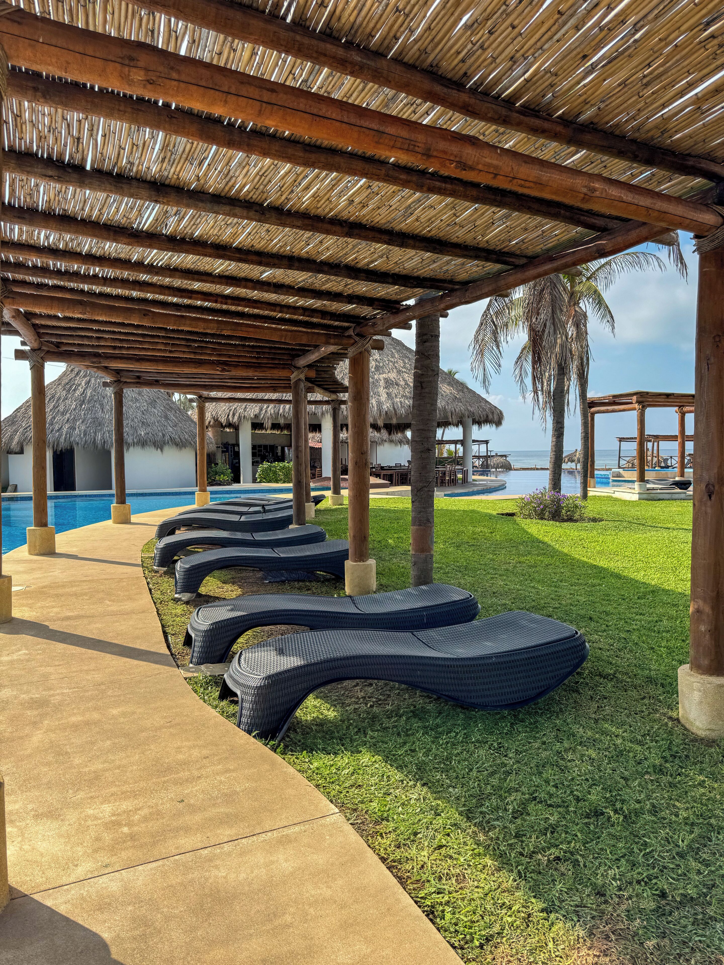 Zona junto a la piscina con sillones de descanso, una estructura de techo de paja y vistas al mar.