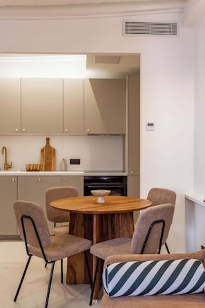 Cozinha moderna com uma mesa de madeira redonda e quatro cadeiras, forno embutido, bancada pequena com pia e objetos decorativos.