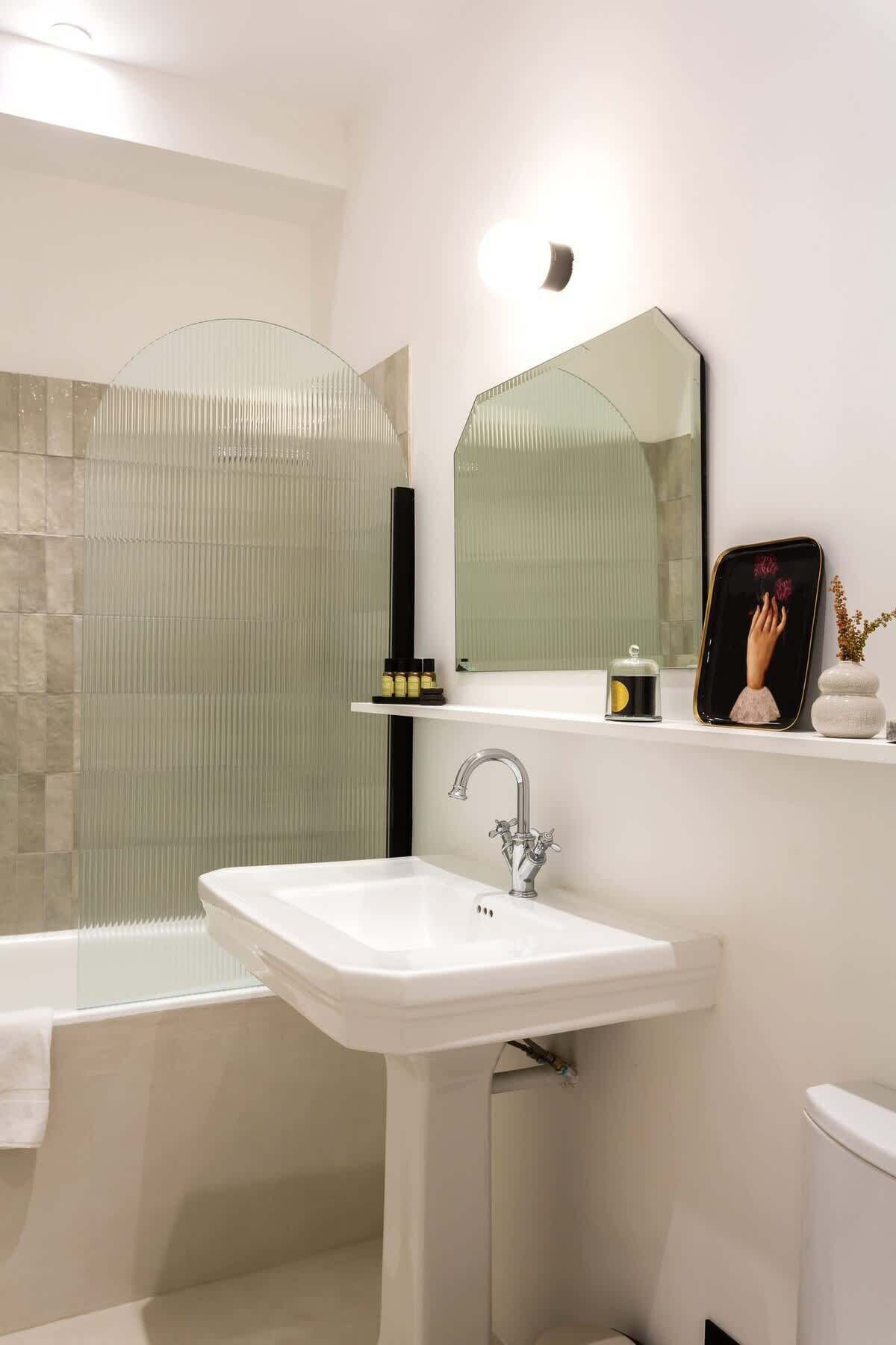 Een moderne badkamer met een witte wastafel, een grote spiegel en een douchecabine van glas.