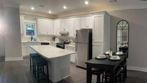 Una cocina moderna con armarios blancos, una isla grande y una zona de comedor con mesa y sillas.
