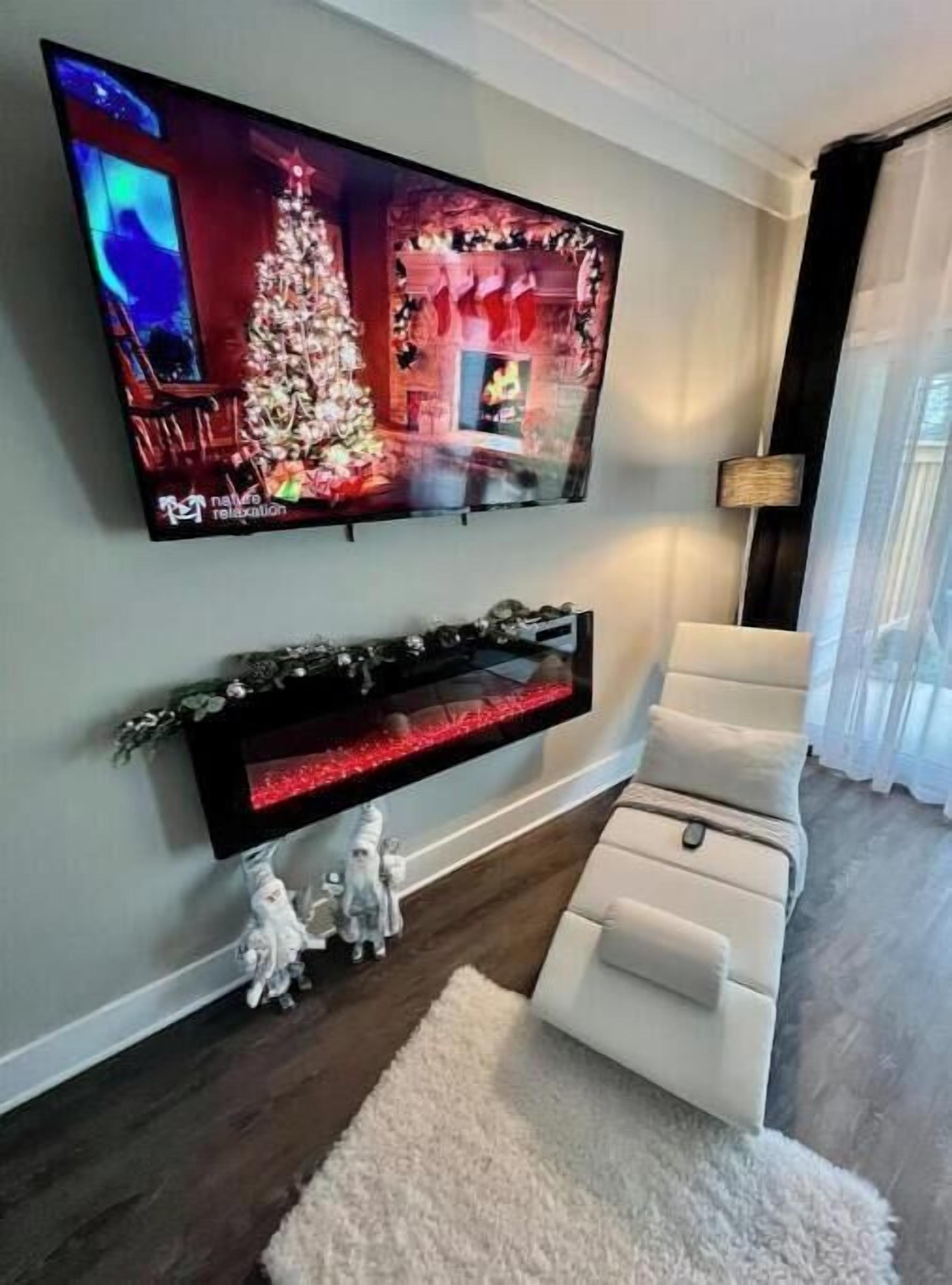 A living room with a flat-screen TV mounted on the wall, a white sofa, and a small fireplace below the TV.