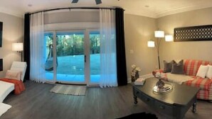 Ein modernes Wohnzimmer mit einer gebogenen Glasdoor, die auf einen Balkon führt, einem wandmontierten Flachbildfernseher, einem Sofa und einem Couchtisch.