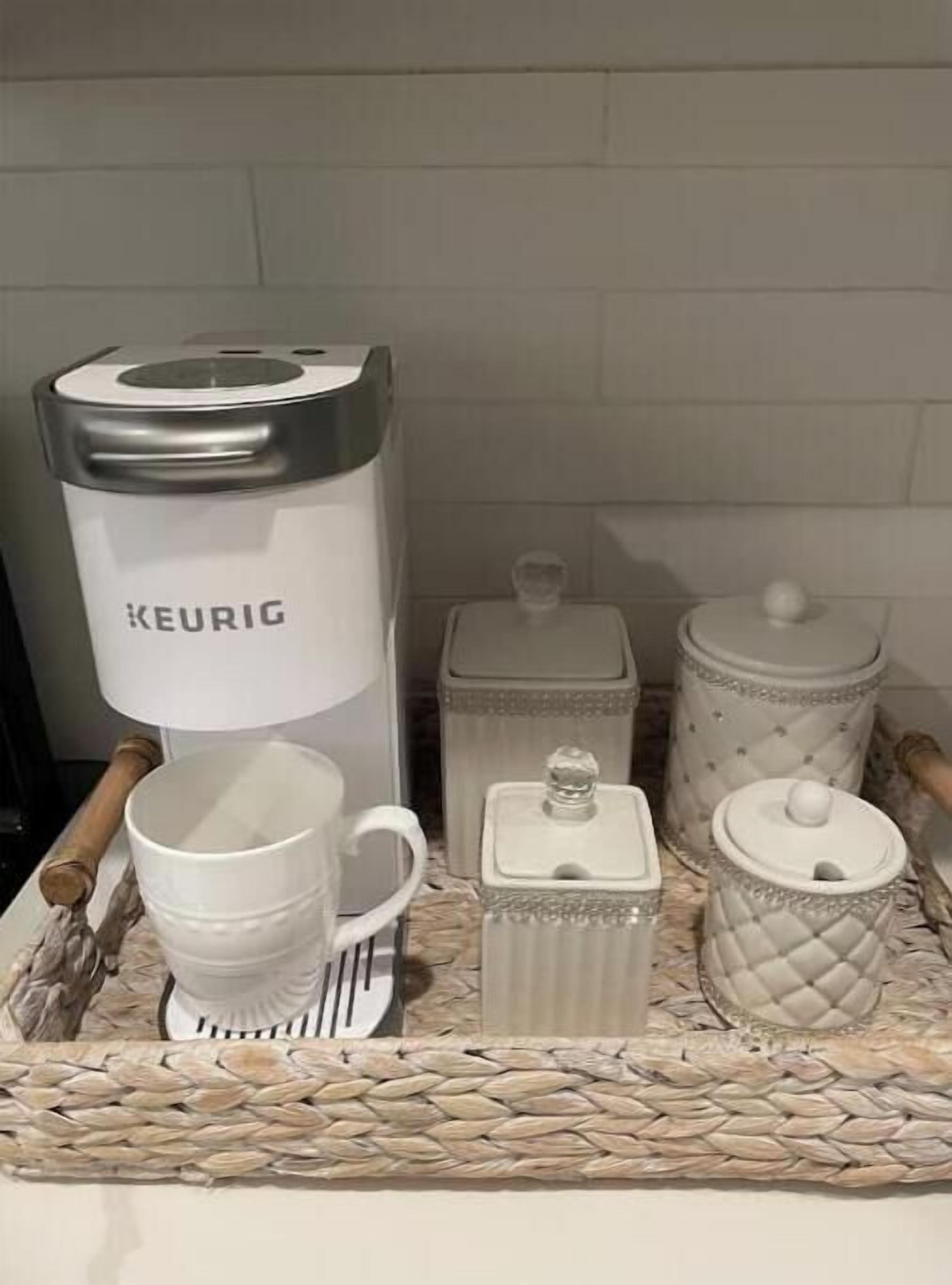 Una bandeja con una cafetera Keurig, una taza blanca, una tetera blanca y dos recipientes blancos.