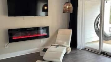 Un salon moderne avec un téléviseur à écran plat fixé au mur, un canapé en cuir blanc, un petit tapis et un ventilateur de plafond.