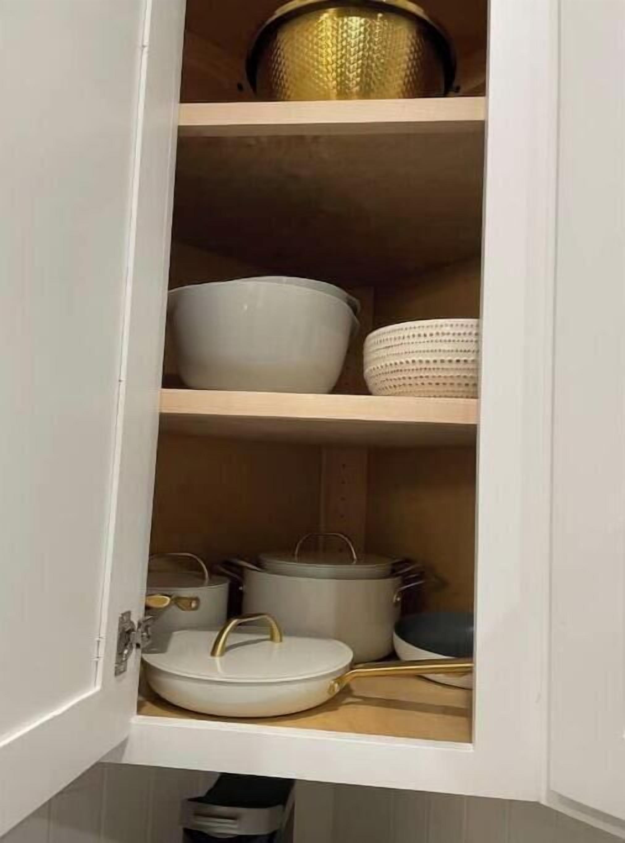 Un meuble de cuisine dont les étagères intérieures sont blanches, et qui contient des bols blancs, une casserole blanche et une poêle blanche.