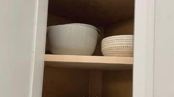 Un meuble de cuisine dont les étagères intérieures sont blanches, et qui contient des bols blancs, une casserole blanche et une poêle blanche.