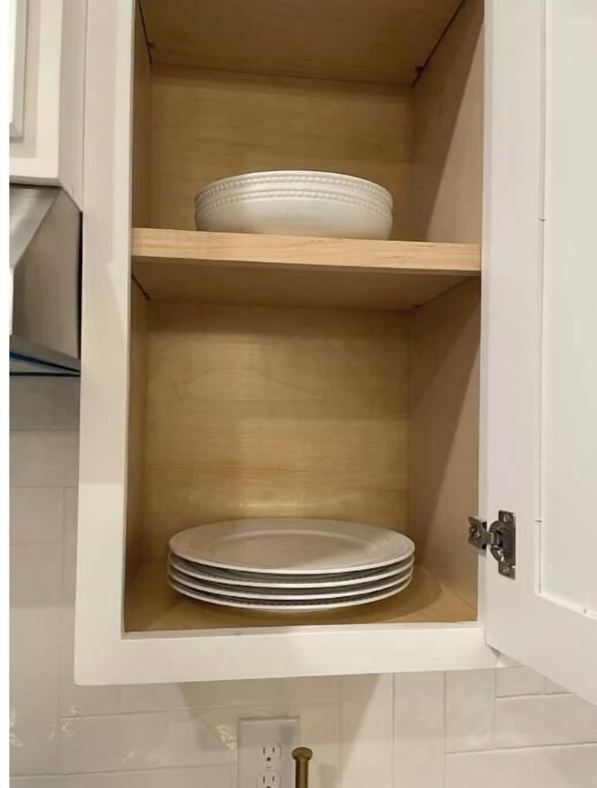 Un armario de cocina con dos repisas, una con una pila de platos y la otra con un solo plato.