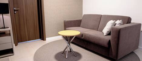 A modern living room with a brown sofa, a small round table, and a television on a stand.