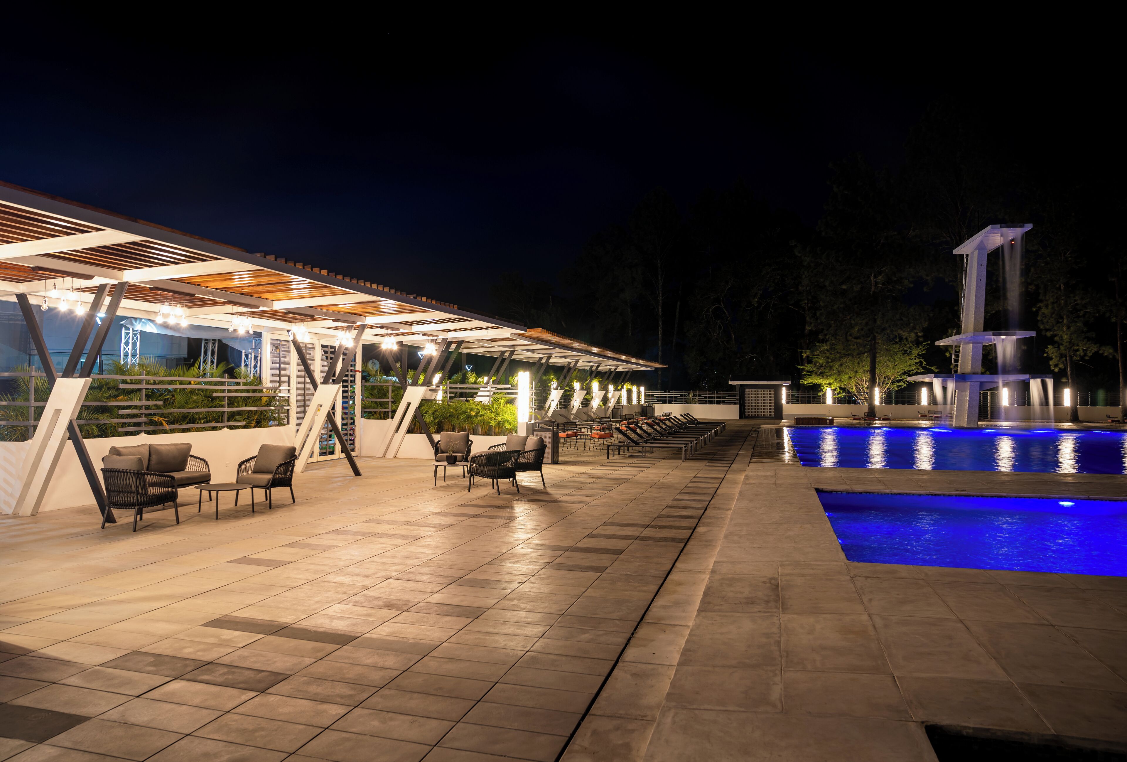 An outdoor pool area with lounge chairs and a covered seating area at night.