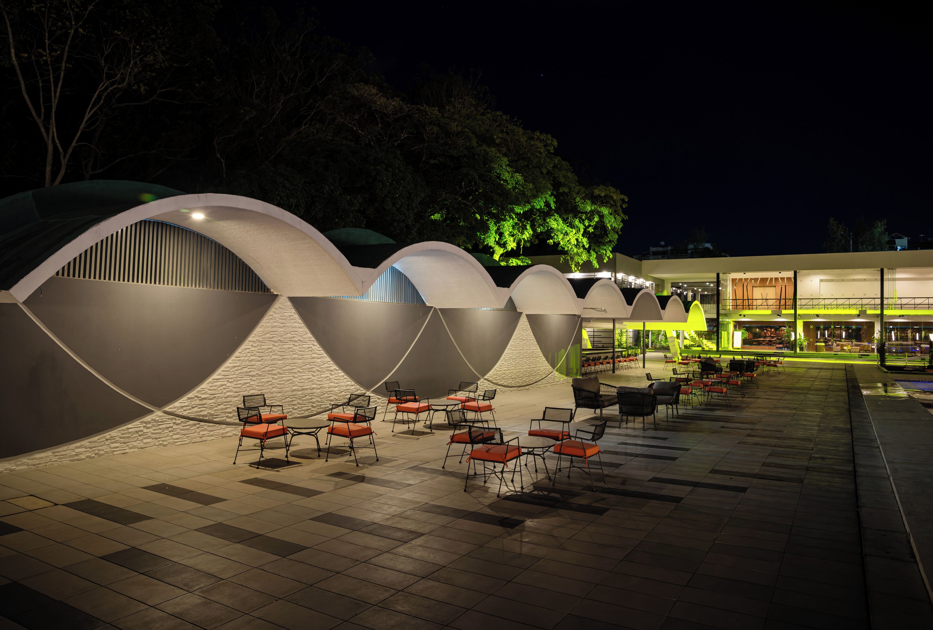 A modern outdoor seating area with multiple tables and chairs, surrounded by uniquely shaped structures with curved roofs.