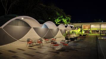 A modern outdoor seating area with multiple tables and chairs, surrounded by uniquely shaped structures with curved roofs.