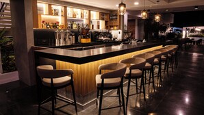 Eine moderne Bar mit einer langen Theke, mehreren Barhocker und einer Auswahl an Flaschen und Gläsern in Regalen.