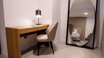 Habitación de hotel moderna con escritorio de madera, una silla, lámpara de escritorio y un espejo grande que refleja la cama y una silla.