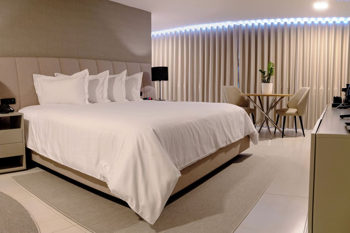 A modern hotel room with a large bed, bedside tables with lamps, a small desk, and a chair.