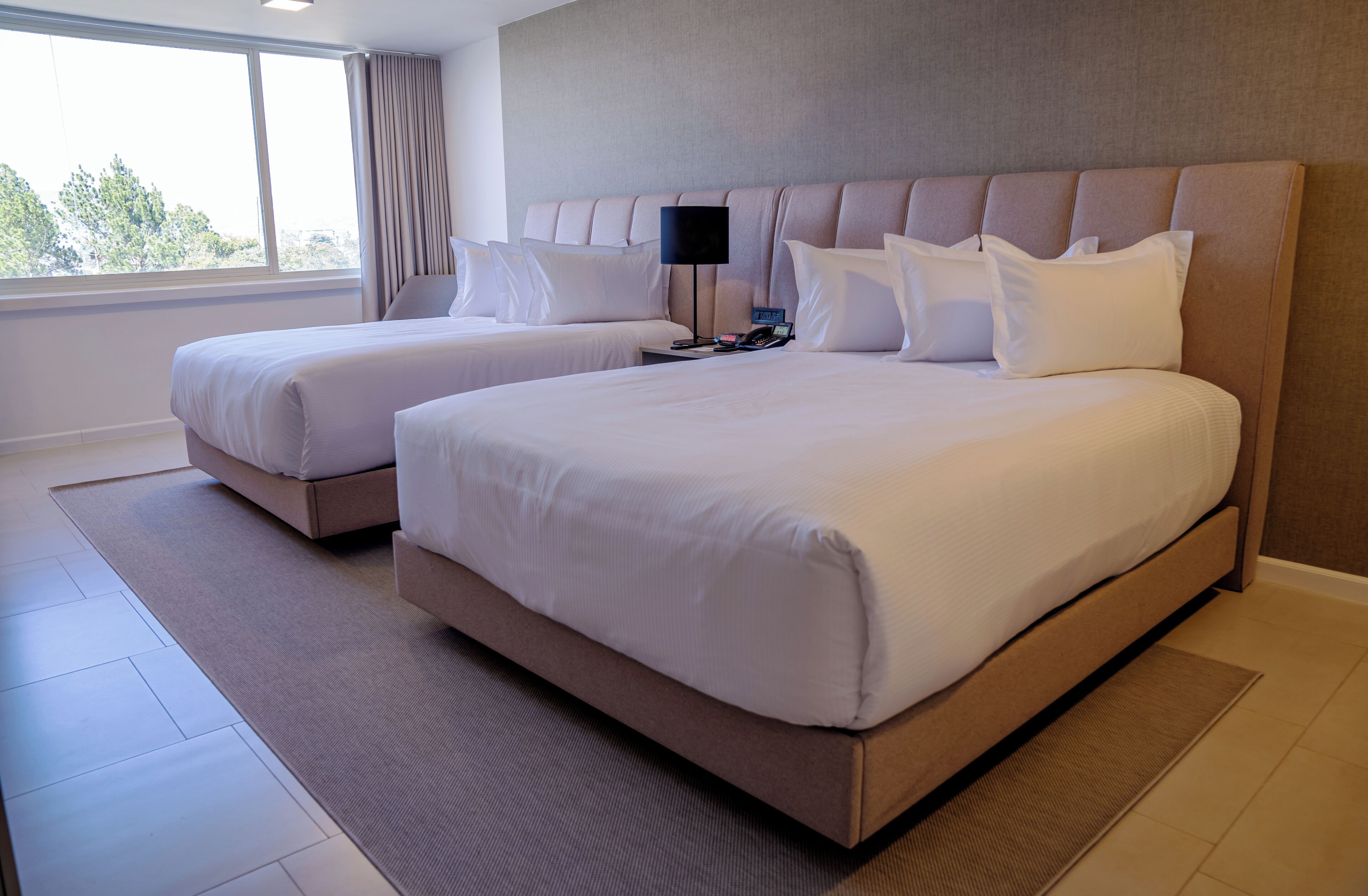 Habitación de hotel con dos camas, un ventanal grande y un diseño moderno.