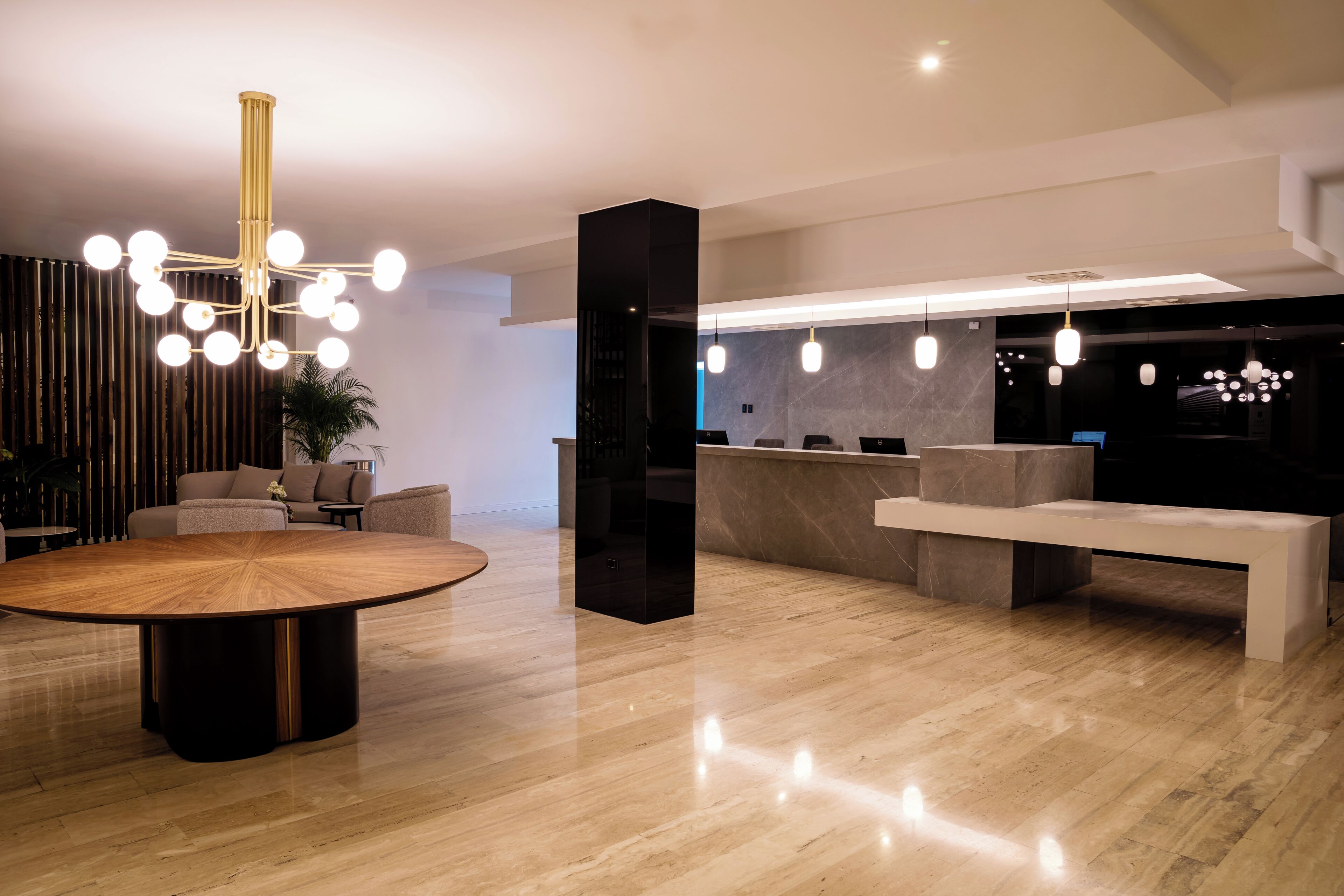 A modern lobby with a round wooden table, a black reception desk, and a large chandelier.
