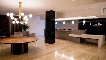 A modern lobby with a round wooden table, a black reception desk, and a large chandelier.