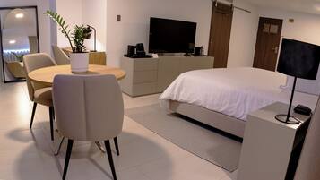 A modern hotel room with a bed, a desk, a chair, a television, a coffee maker, and a plant.