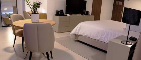 A modern hotel room with a bed, a desk, a chair, a television, a coffee maker, and a plant.