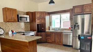 Cocina con armarios de madera, encimera de granito, electrodomésticos de acero inoxidable y ventana que proporciona luz natural.