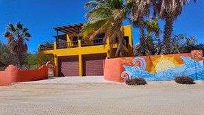 Un bâtiment jaune avec une porte de garage rouge, des palmiers et une fresque murale.