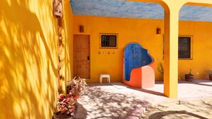 Un bâtiment jaune avec une porte en bois, une structure bleue et orange, et des plantes en pot.