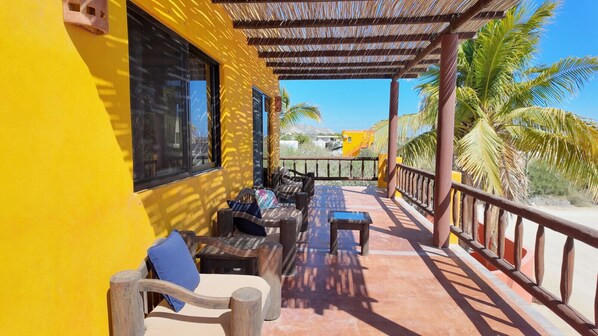 A yellow building with a covered outdoor seating area, wooden furniture, and a view of palm trees and a bridge.