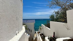 Vista costera con cielo despejado, un edificio con tejado de azulejos y un camino que lleva al mar.