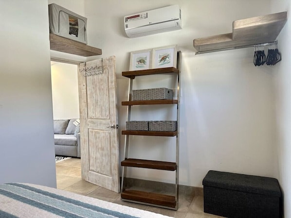 A hallway with a wooden ladder shelf, a grey bench, and a door leading to a living area.
