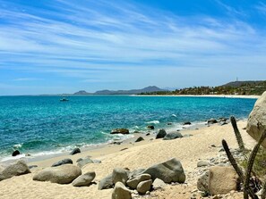Enjoy the serene beach scene with clear waters, sandy shore, and scenic views of the surrounding mountains.
