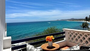 Un balcón con vistas al océano, una mesa de madera con un florero y una barandilla blanca.