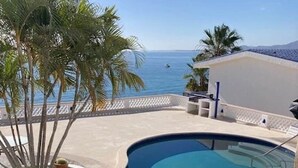 Una piscina curvada con vistas despejadas al océano, rodeada de palmeras y un edificio blanco.