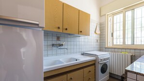 A kitchen with wooden cabinets, a double sink, a built-in oven, and a window with blinds. - 4173 Villetta Ambra by Barbarhouse (Porto Cesareo)