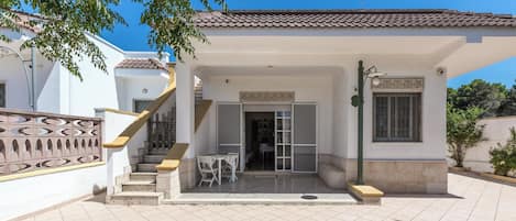 A two-story house with a tiled patio, a staircase, and a small outdoor seating area.