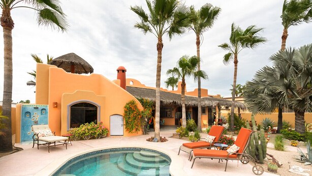 A pool area with lounge chairs, palm trees, and a building with a thatched roof.