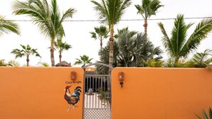 An orange wall with a gate, a rooster mural, and palm trees.
