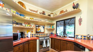 A kitchen with wooden cabinets, a stainless steel refrigerator, a stove, and a window with a view of greenery.