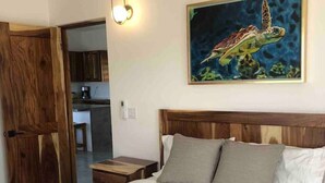 Un dormitorio con puerta de madera, una cama con ropa blanca, cabecero y un cuadro de tortuga marina en la pared.