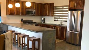 Una cocina moderna con armarios de madera, un refrigerador de acero inoxidable, horno empotrado e isla central con taburetes.