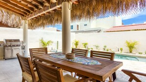 An outdoor dining area with a wooden table and chairs, a grill, and a pool in the background. - Walkable Convenient in Downtown Los Barriles (Los Barriles)